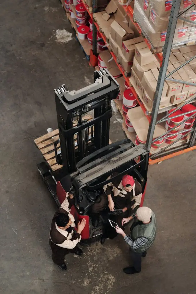 Warehouse employees discussing logistics around a forklift in an industrial setting.